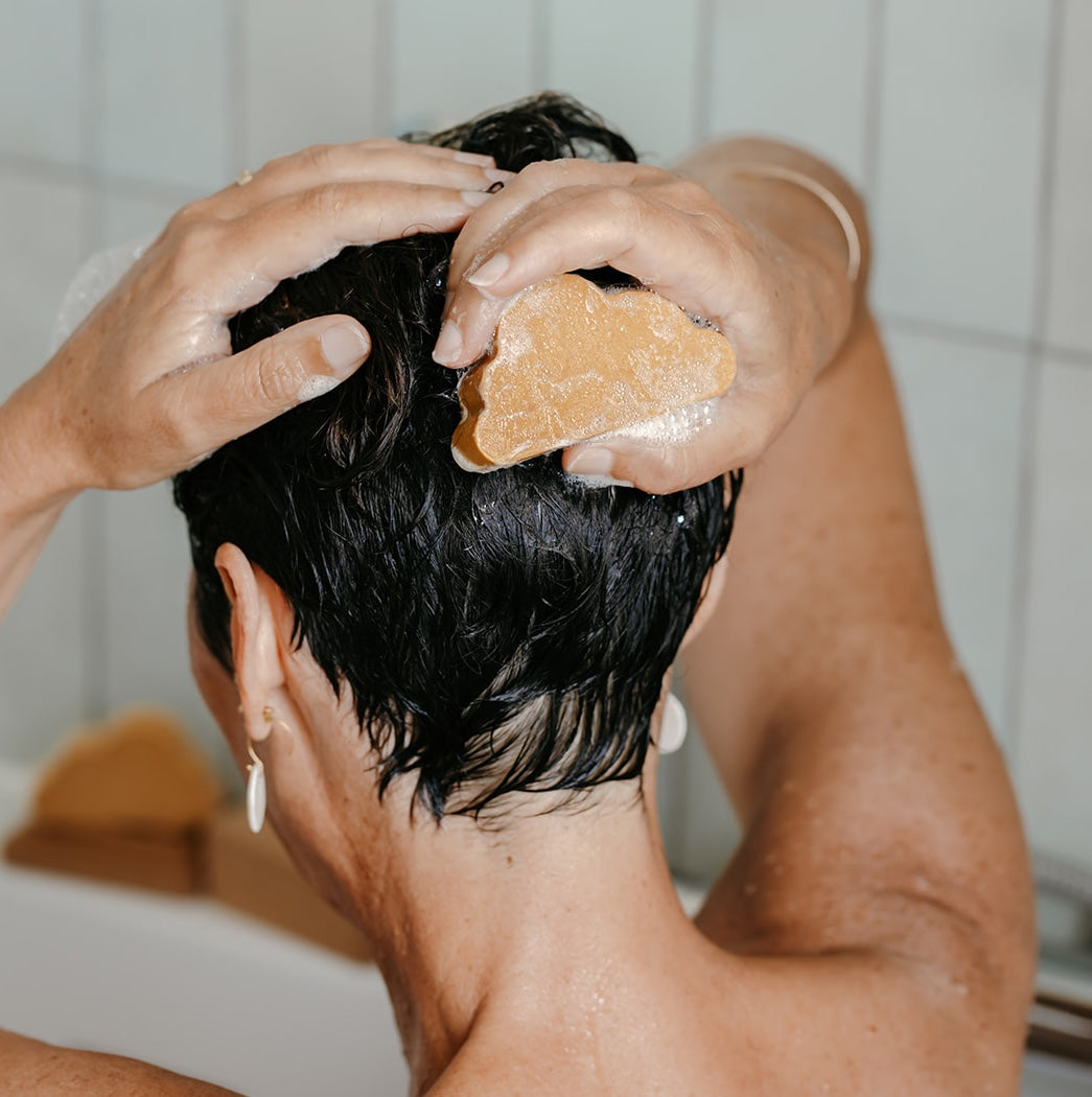 Femme aux cheveux courts qui fait mousser son shampoing solide en forme de nuage sur ses cheveux