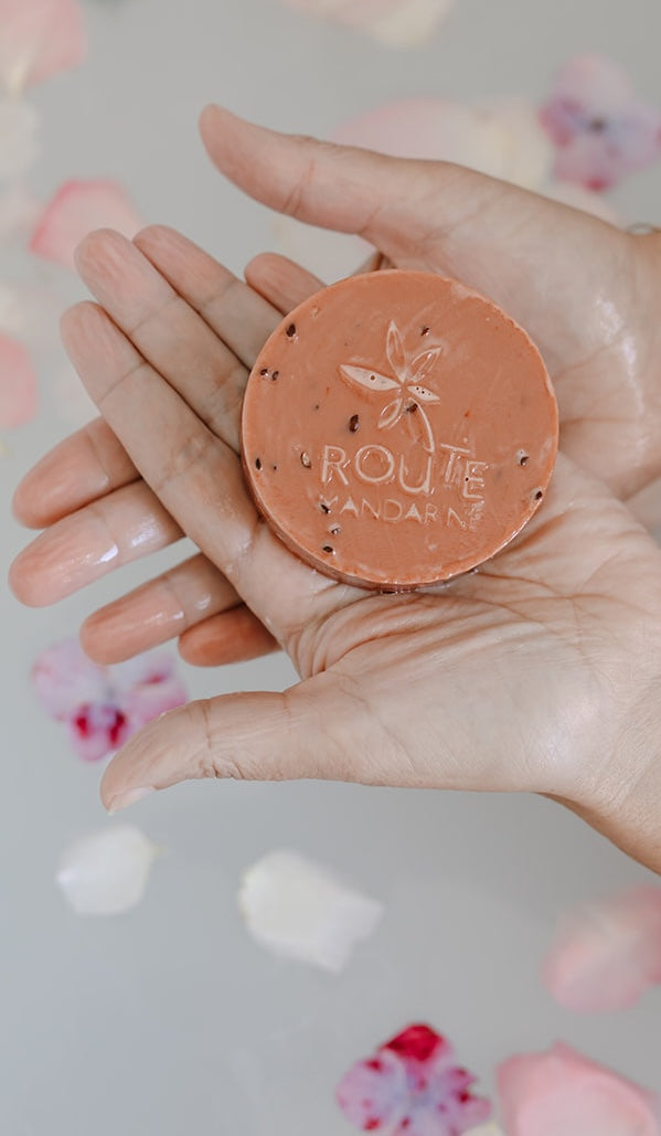 Savon Samouraï dans les mains d'une femme au dessus de l'eau lactée d'une baignoire et de pétales de fleurs